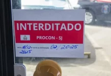 Placa de ‘interditado pelo Procon de São José’ colada na porta de vidro de um comércio, representando suspensão de alvará em São José.