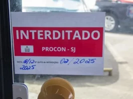 Placa de ‘interditado pelo Procon de São José’ colada na porta de vidro de um comércio, representando suspensão de alvará em São José.