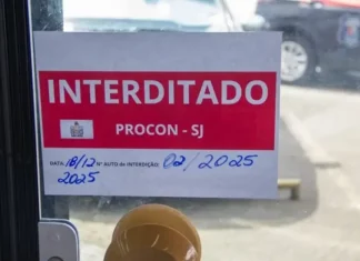 Placa de ‘interditado pelo Procon de São José’ colada na porta de vidro de um comércio, representando suspensão de alvará em São José.