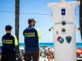 MPSC recomenda suspensão imediata de voluntários de segurança em Florianópolis Voluntários de segurança em Florianópolis observam movimento na praia ao lado de torre de monitoramento com símbolos da Guarda Municipal e da Polícia Militar.