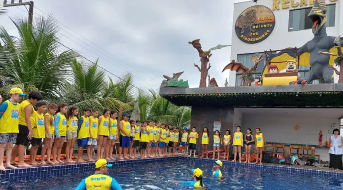 Crianças participam de atividade do Projeto Golfinho SC em piscina, acompanhadas por instrutores, aprendendo práticas de prevenção de afogamentos e segurança na água.