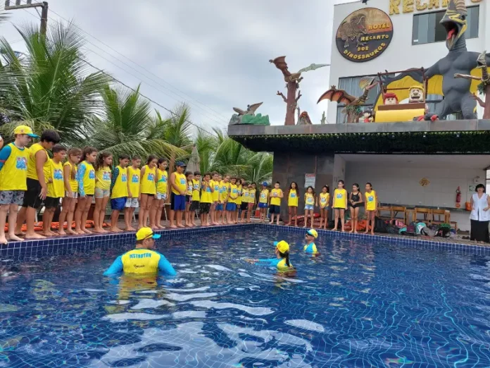 Crianças participam de atividade do Projeto Golfinho SC em piscina, acompanhadas por instrutores, aprendendo práticas de prevenção de afogamentos e segurança na água.