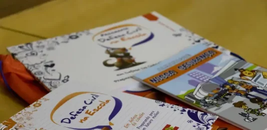 Programa Defesa Civil na Escola alcança 87 mil alunos em SC Cadernos e materiais do Programa Defesa Civil na Escola sobre mesa, utilizados para ensinar alunos sobre prevenção de desastres e segurança nas escolas.