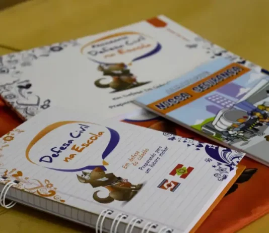 Cadernos e materiais do Programa Defesa Civil na Escola sobre mesa, utilizados para ensinar alunos sobre prevenção de desastres e segurança nas escolas.