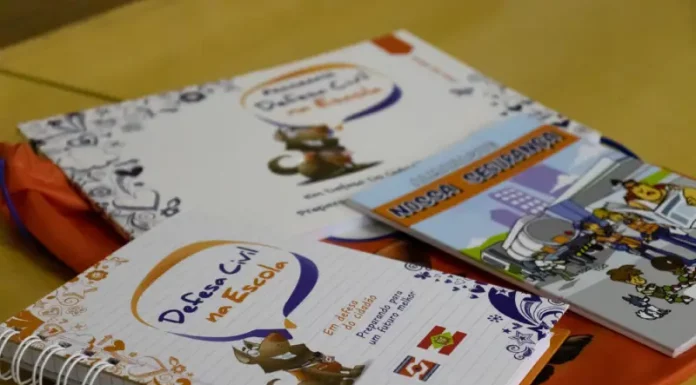 Programa Defesa Civil na Escola alcança 87 mil alunos em SC Cadernos e materiais do Programa Defesa Civil na Escola sobre mesa, utilizados para ensinar alunos sobre prevenção de desastres e segurança nas escolas.