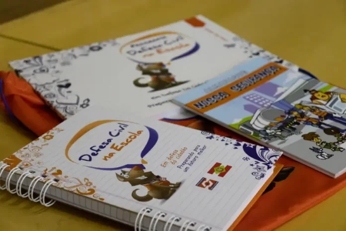 Defesa-civil-na-escola-2 Cadernos e materiais do Programa Defesa Civil na Escola sobre mesa, utilizados para ensinar alunos sobre prevenção de desastres e segurança nas escolas.