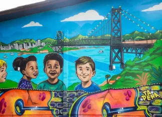 Mural de grafite no Jardim Botânico de Florianópolis retrata crianças e a Ponte Hercílio Luz, simbolizando a participação infantil em projeto de arte e cidadania.