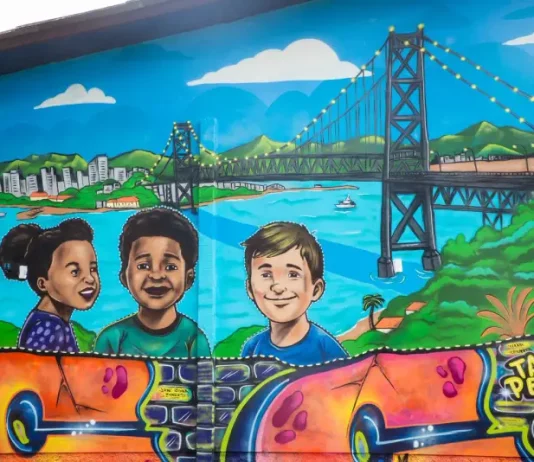 Mural de grafite no Jardim Botânico de Florianópolis retrata crianças e a Ponte Hercílio Luz, simbolizando a participação infantil em projeto de arte e cidadania.