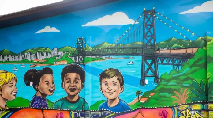 Mural de grafite no Jardim Botânico de Florianópolis retrata crianças e a Ponte Hercílio Luz, simbolizando a participação infantil em projeto de arte e cidadania.