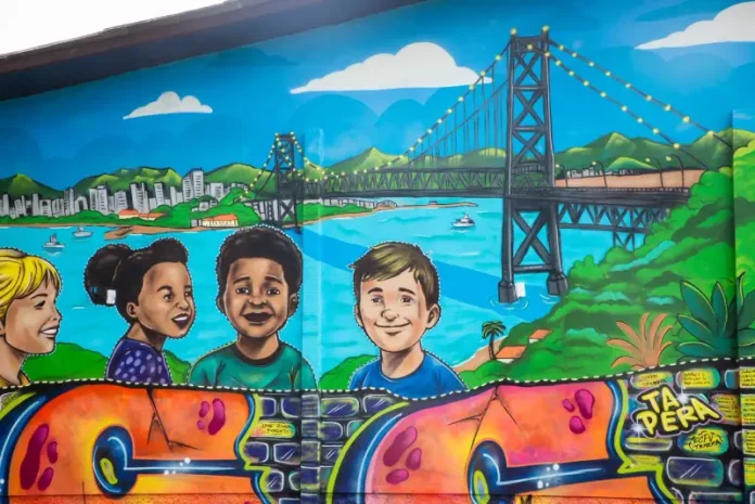 Mural de grafite no Jardim Botânico de Florianópolis retrata crianças e a Ponte Hercílio Luz, simbolizando a participação infantil em projeto de arte e cidadania.