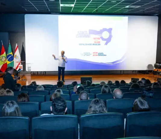 Governador Jorginho Mello durante apresentação no lançamento do Santa Catarina Canta 2026 em auditório, com público presente, destacando a abertura das inscrições e a divulgação do festival de música no estado.