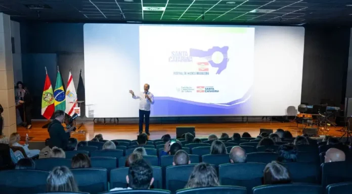 Governador Jorginho Mello durante apresentação no lançamento do Santa Catarina Canta 2026 em auditório, com público presente, destacando a abertura das inscrições e a divulgação do festival de música no estado.