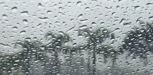 Gotas de chuva intensa sobre vidro com paisagem desfocada ao fundo, ilustrando o tempo instável e o volume elevado de precipitação em Santa Catarina.