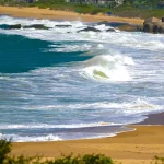 Mar agitado com ondas fortes atingindo a faixa de areia, ilustrando os efeitos do ciclone extratropical e o risco de ressaca no litoral de Santa Catarina.