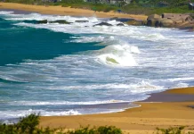 Mar agitado com ondas fortes atingindo a faixa de areia, ilustrando os efeitos do ciclone extratropical e o risco de ressaca no litoral de Santa Catarina.