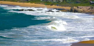 Mar agitado com ondas fortes atingindo a faixa de areia, ilustrando os efeitos do ciclone extratropical e o risco de ressaca no litoral de Santa Catarina.