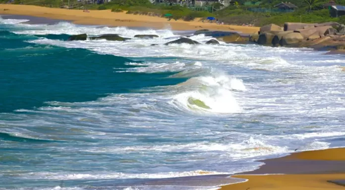 Mar agitado com ondas fortes atingindo a faixa de areia, ilustrando os efeitos do ciclone extratropical e o risco de ressaca no litoral de Santa Catarina.