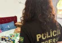 Policial federal durante ação contra comércio ilegal de medicamentos, com remédios apreendidos sobre cama em residência.