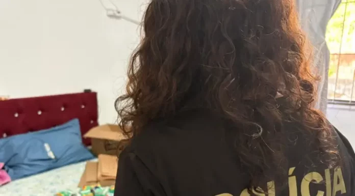 Policial federal durante ação contra comércio ilegal de medicamentos, com remédios apreendidos sobre cama em residência.