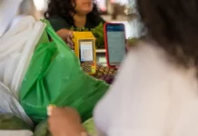 Cliente realiza pagamento por aproximação em maquininha enquanto funcionária entrega compras, ilustrando o movimento do comércio de Santa Catarina.