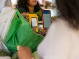 Cliente realiza pagamento por aproximação em maquininha enquanto funcionária entrega compras, ilustrando o movimento do comércio de Santa Catarina.