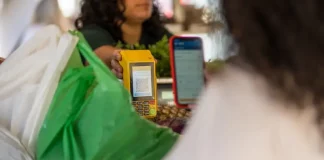 Cliente realiza pagamento por aproximação em maquininha enquanto funcionária entrega compras, ilustrando o movimento do comércio de Santa Catarina.
