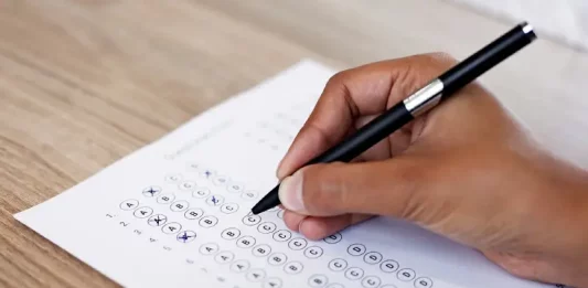 Mão preenchendo gabarito de prova, simulando participação no concurso da InvestSC.