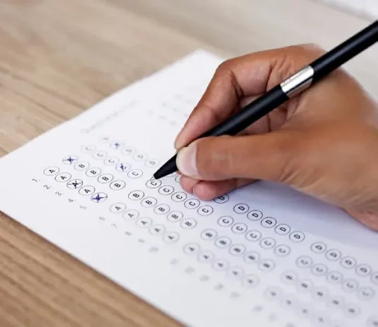 Mão preenchendo gabarito de prova, simulando participação no concurso da InvestSC.