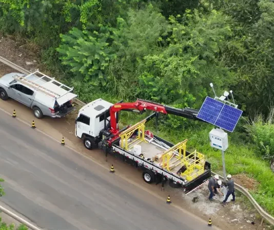 Instalação de estações meteorológicas e hidrológicas às margens de rodovia, com uso de caminhão guindaste e painel solar, para monitoramento do clima e prevenção de desastres em tempo real.