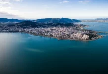 Vista aérea de Florianópolis, mostrando a área urbana cercada pelo mar, utilizada para ilustrar a cidade que aderiu à Declaração de Belém e adotou medidas de compras públicas sustentáveis.