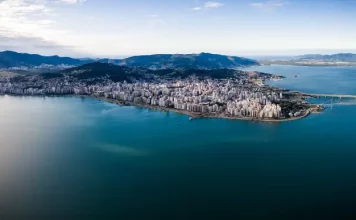 Vista aérea de Florianópolis, mostrando a área urbana cercada pelo mar, utilizada para ilustrar a cidade que aderiu à Declaração de Belém e adotou medidas de compras públicas sustentáveis.
