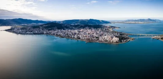 Vista aérea de Florianópolis, mostrando a área urbana cercada pelo mar, utilizada para ilustrar a cidade que aderiu à Declaração de Belém e adotou medidas de compras públicas sustentáveis.