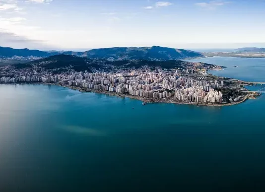Vista aérea de Florianópolis, mostrando a área urbana cercada pelo mar, utilizada para ilustrar a cidade que aderiu à Declaração de Belém e adotou medidas de compras públicas sustentáveis.