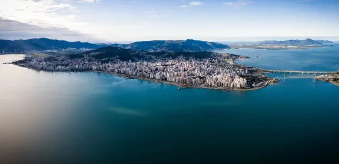 Vista aérea de Florianópolis, mostrando a área urbana cercada pelo mar, utilizada para ilustrar a cidade que aderiu à Declaração de Belém e adotou medidas de compras públicas sustentáveis.