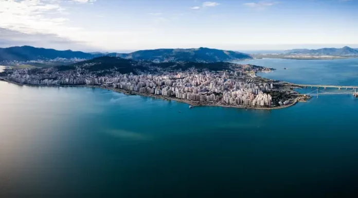 Vista aérea de Florianópolis, mostrando a área urbana cercada pelo mar, utilizada para ilustrar a cidade que aderiu à Declaração de Belém e adotou medidas de compras públicas sustentáveis.