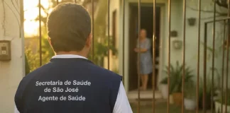 Imagem gerada por IA mostra um homem com colete de agente de saúde da Secretaria de São José em frente a uma residência, ilustrando a ação de golpistas que se passam por profissionais para aplicar fraudes.