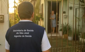 Imagem gerada por IA mostra um homem com colete de agente de saúde da Secretaria de São José em frente a uma residência, ilustrando a ação de golpistas que se passam por profissionais para aplicar fraudes.