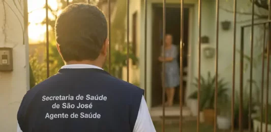 Imagem gerada por IA mostra um homem com colete de agente de saúde da Secretaria de São José em frente a uma residência, ilustrando a ação de golpistas que se passam por profissionais para aplicar fraudes.