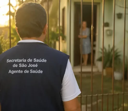 Imagem gerada por IA mostra um homem com colete de agente de saúde da Secretaria de São José em frente a uma residência, ilustrando a ação de golpistas que se passam por profissionais para aplicar fraudes.
