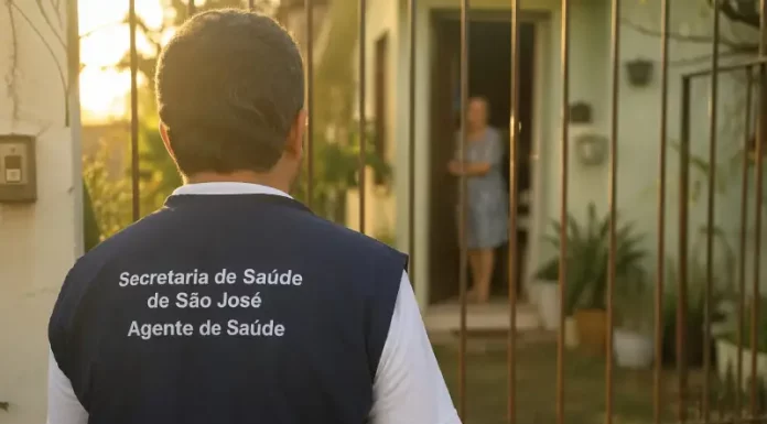 Imagem gerada por IA mostra um homem com colete de agente de saúde da Secretaria de São José em frente a uma residência, ilustrando a ação de golpistas que se passam por profissionais para aplicar fraudes.