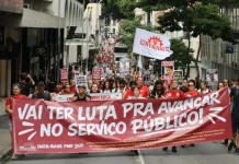 Servidores públicos participam de manifestação durante a greve servidores Florianópolis, com faixa do Sintrasem e cartazes com reivindicações da categoria em rua central.