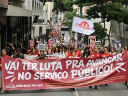 Servidores públicos participam de manifestação durante a greve servidores Florianópolis, com faixa do Sintrasem e cartazes com reivindicações da categoria em rua central.