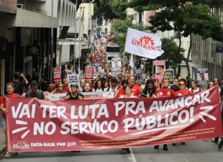 Servidores públicos participam de manifestação durante a greve servidores Florianópolis, com faixa do Sintrasem e cartazes com reivindicações da categoria em rua central.
