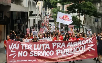 Servidores públicos participam de manifestação durante a greve servidores Florianópolis, com faixa do Sintrasem e cartazes com reivindicações da categoria em rua central.