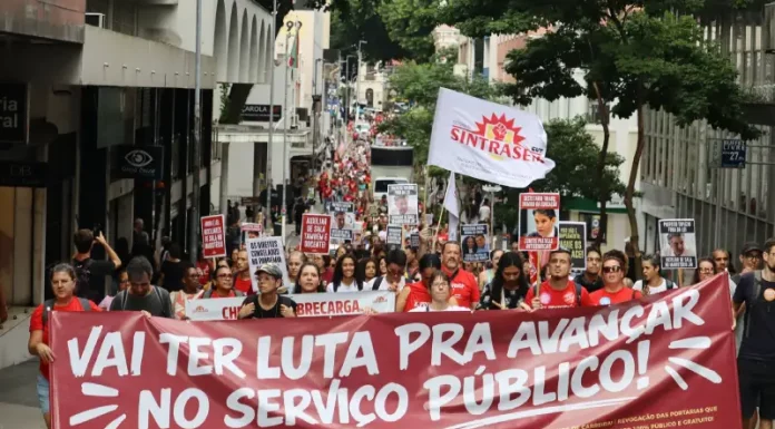 Servidores públicos participam de manifestação durante a greve servidores Florianópolis, com faixa do Sintrasem e cartazes com reivindicações da categoria em rua central.