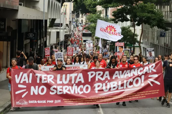 Servidores públicos participam de manifestação durante a greve servidores Florianópolis, com faixa do Sintrasem e cartazes com reivindicações da categoria em rua central.