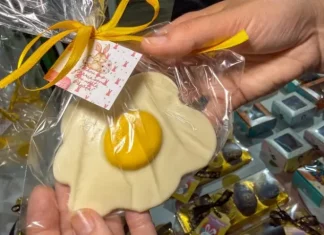 Pessoa segura um doce artesanal em formato de ovo frito, embalado para presente, representando produtos criativos de pequenos negócios para a Páscoa.
