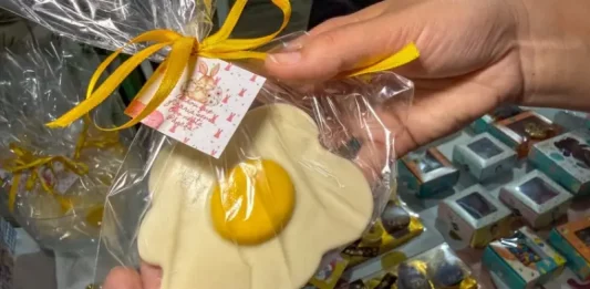 Pessoa segura um doce artesanal em formato de ovo frito, embalado para presente, representando produtos criativos de pequenos negócios para a Páscoa.