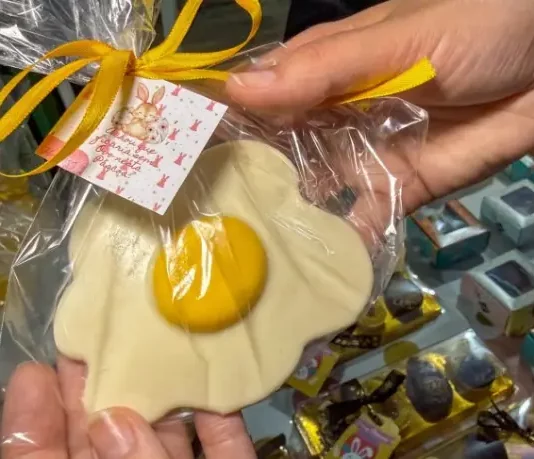 Pessoa segura um doce artesanal em formato de ovo frito, embalado para presente, representando produtos criativos de pequenos negócios para a Páscoa.
