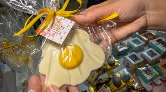 Pessoa segura um doce artesanal em formato de ovo frito, embalado para presente, representando produtos criativos de pequenos negócios para a Páscoa.